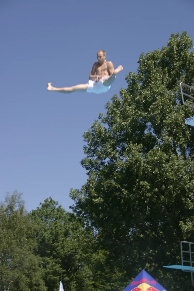 Christian „Elvis“ Guth mit weit geöffneten Beinen in der Luft vor Bäumen und blauem Himmel, Archiv 2005.