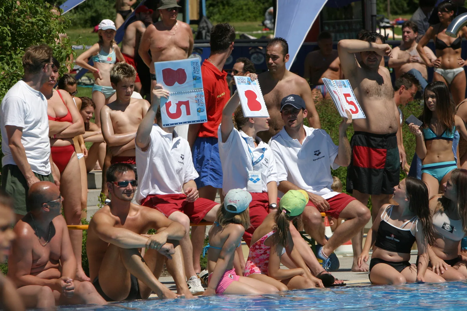 Drei Jurymitglieder mit roten Wertungstafeln inmitten des Freibadpublikums, 2005.