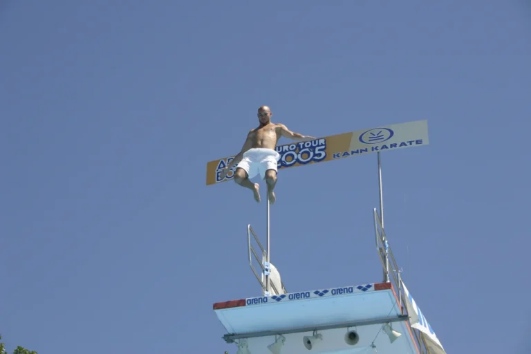 Ein Springer mit seitlich geöffneten Armen und angewinkelten Beinen vor blauem Himmel und Eurotour-Schild, 2005.