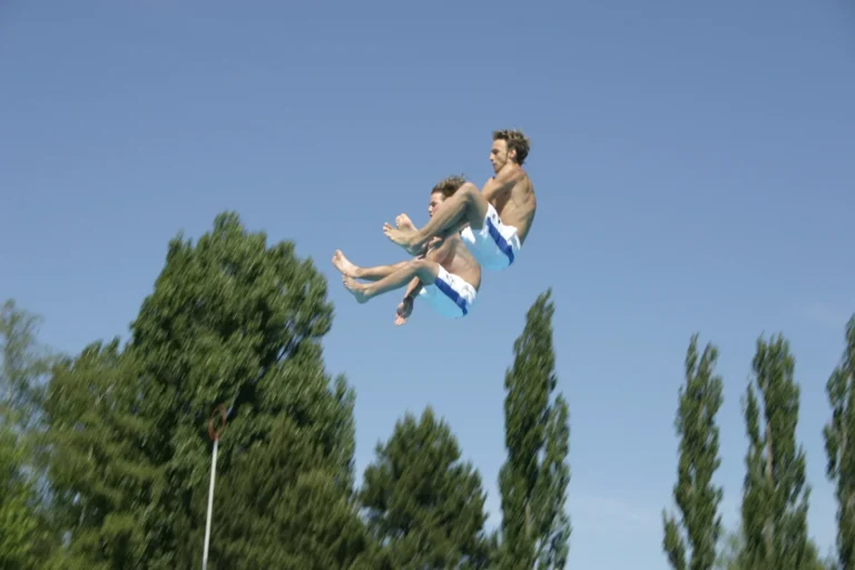 Zwei Springer gleichzeitig in der Luft vor Bäumen und blauem Himmel, 2005.