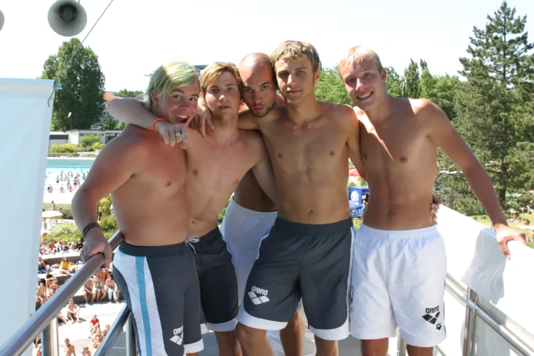 Fünf Teammitglieder stehen gemeinsam auf der Plattform des Sprungturms über dem sonnigen Freibad, 2005.