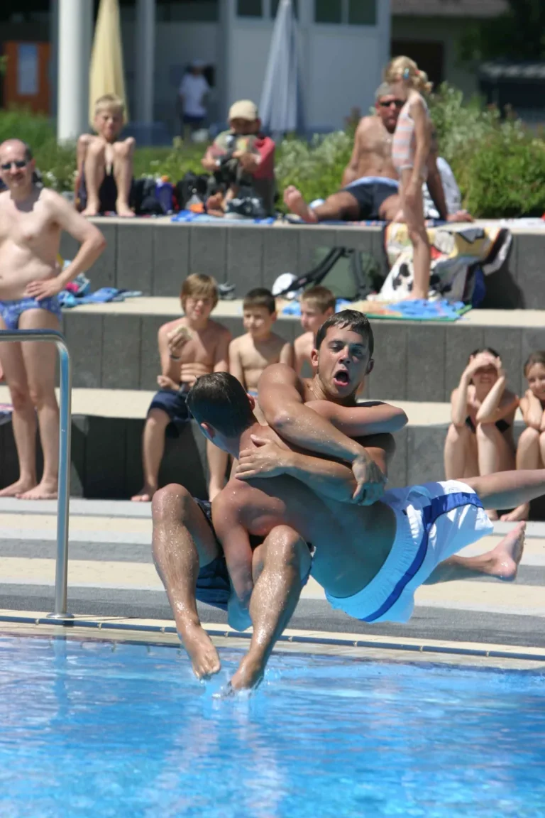 Zwei Teammitglieder gemeinsam beim Sprung am Beckenrand vor Zuschauern, 2005.