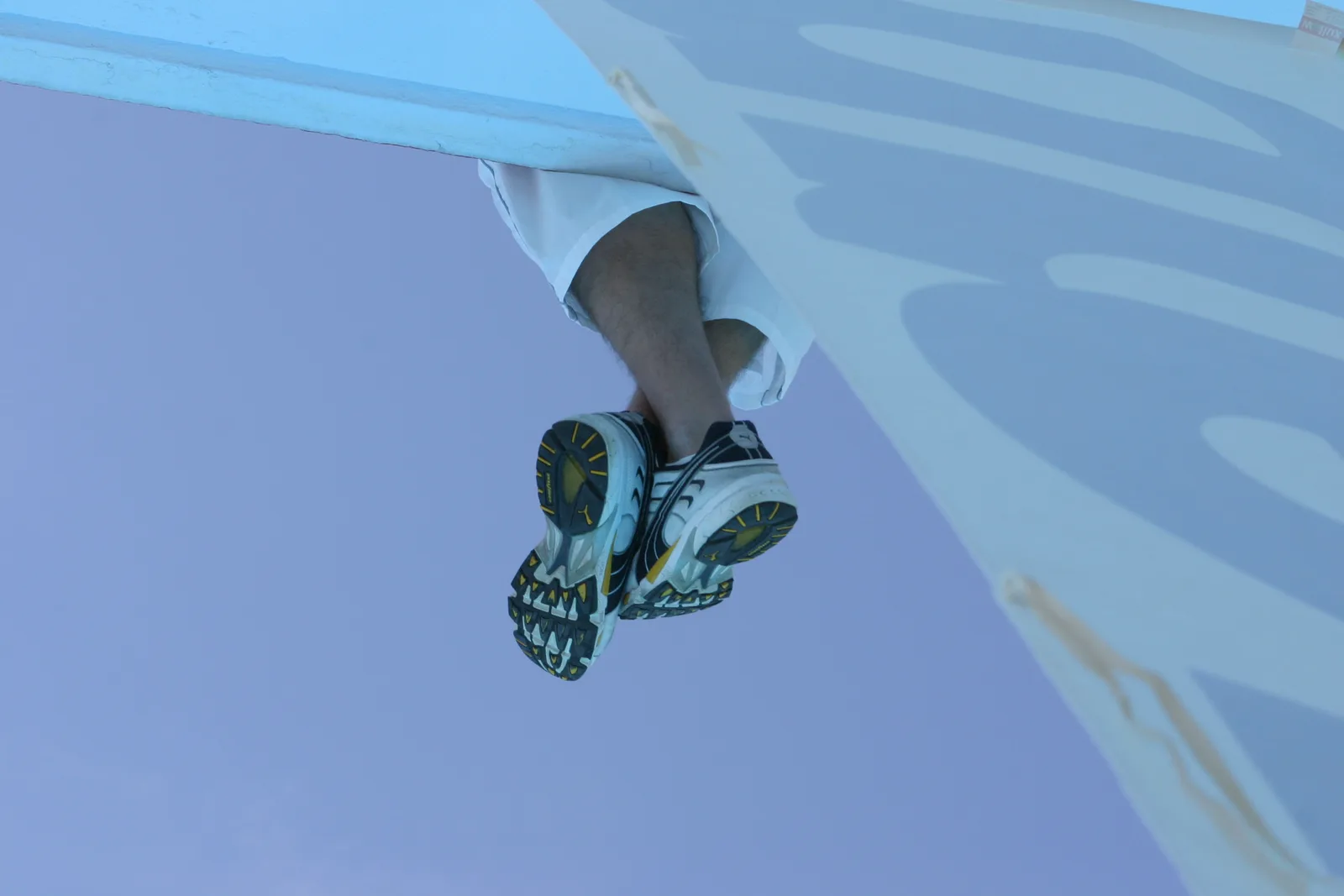 Beine und Sportschuhe einer Person am Sprungturm, von unten vor blauem Himmel fotografiert, 2005.