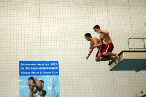 Two divers in red shorts taking off together from an indoor diving platform, 2005.