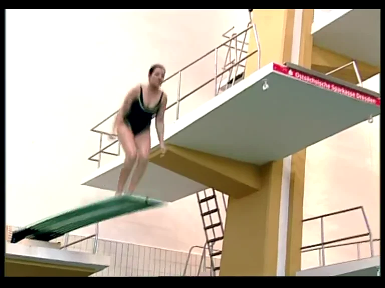 Karen auf einer Sprungplattform in der Schwimmhalle, aus dem Hintergrundfilm zum klassischen Wasserspringen.