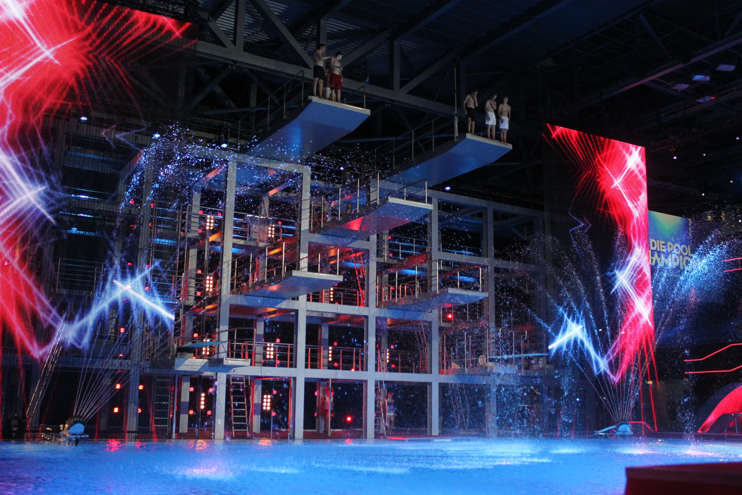Showbühne mit Sprungturm, Fontänen und dem sichtbaren Titel „Die Pool Champions“. Eigene Archivaufnahme, Kameradatum 21. Juni 2013. Kein Foto der August-WM im Sommerbad Neukölln.