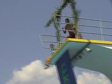 Ein Springer in der Flugphase neben einem Freibad-Sprungturm
