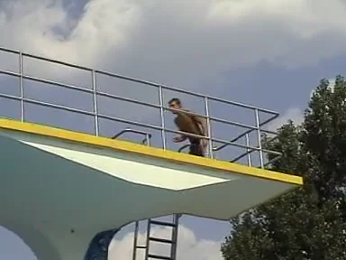 Ein Springer vor blauem Himmel und Publikum am Freibadbecken